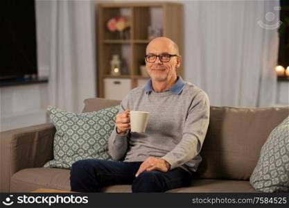 old age, drink and people concept - happy senior man with cup of tea at home in evening. happy senior man with cup of tea at home