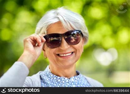 old age, eyewear and people concept - portrait of happy senior woman in sunglasses at summer park. portrait of happy senior woman at summer park