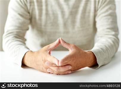 old age, gesture and people concept - close up of senior man hands in triangle of power on table