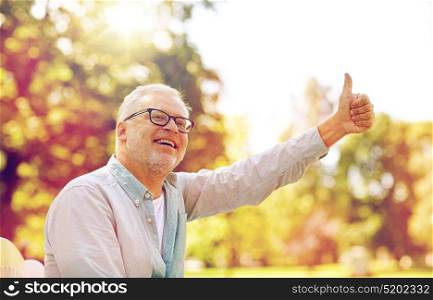 old age, gesture and people concept - happy senior man in glasses sitting at summer park and showing thumbs up. happy senior man showing thumbs up at summer park