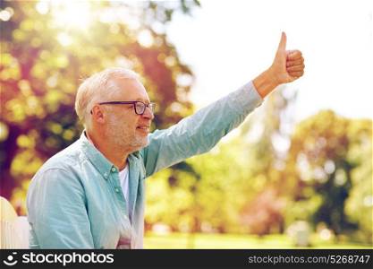 old age, gesture and people concept - happy senior man in glasses sitting at summer park and showing thumbs up. happy senior man showing thumbs up at summer park