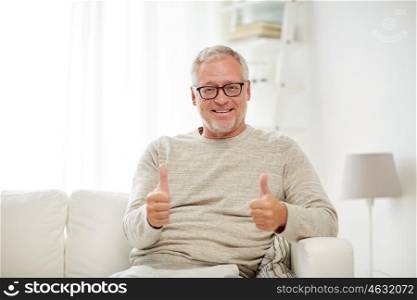 old age, gesture and people concept - smiling senior man in glasses sitting on sofa and showing thumbs up at home