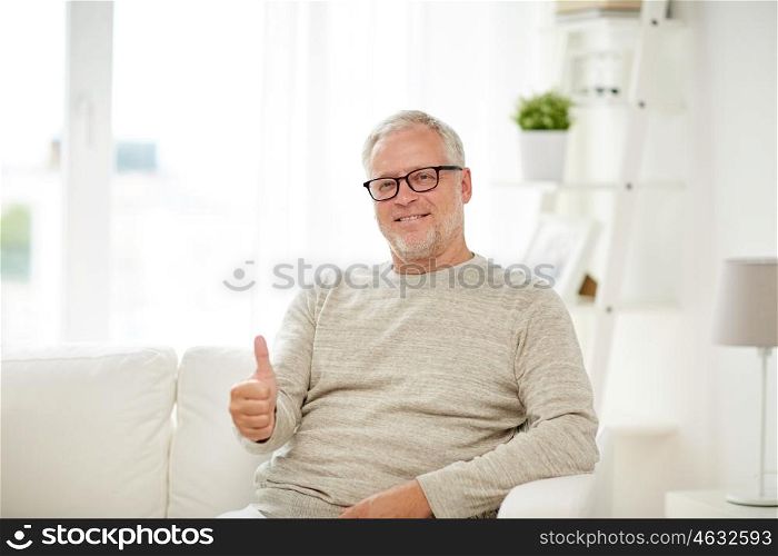 old age, gesture, retirement and people concept - smiling senior man in glasses showing thumbs up at home