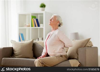 old age, health problem and people concept - senior woman suffering from pain in back or reins at home. senior woman suffering from pain in back at home