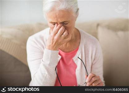 old age, health problem, vision and people concept - close up of senior woman with glasses sitting on sofa and having headache at home. senior woman with glasses having headache at home