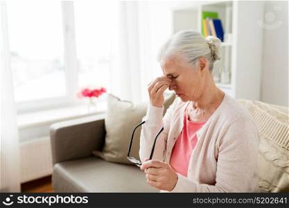 old age, health problem, vision and people concept - senior woman with glasses sitting on sofa and having headache at home. senior woman with glasses having headache at home