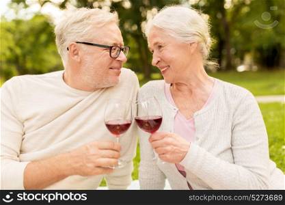 old age, holidays, leisure and people concept - happy senior couple clinking wine glasses at summer park. happy senior couple drinking wine at summer park