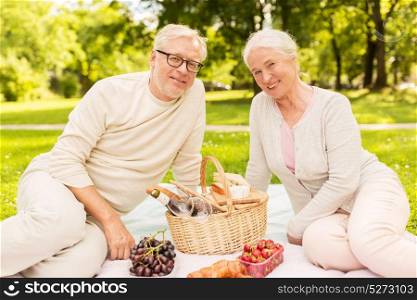 old age, holidays, leisure and people concept - happy senior couple with picnic basket sitting on blanket at summer park. happy senior couple having picnic at summer park