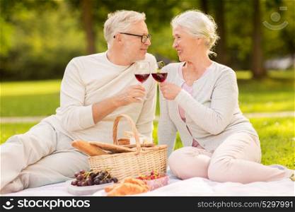 old age, holidays, leisure and people concept - happy senior couple with picnic basket and wine glasses sitting on blanket at summer park. happy senior couple having picnic at summer park