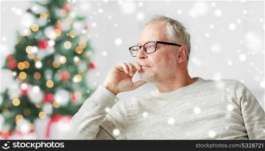 old age, holidays, problem and people concept - senior man in glasses thinking at home over christmas tree background and snow. senior man in glasses thinking
