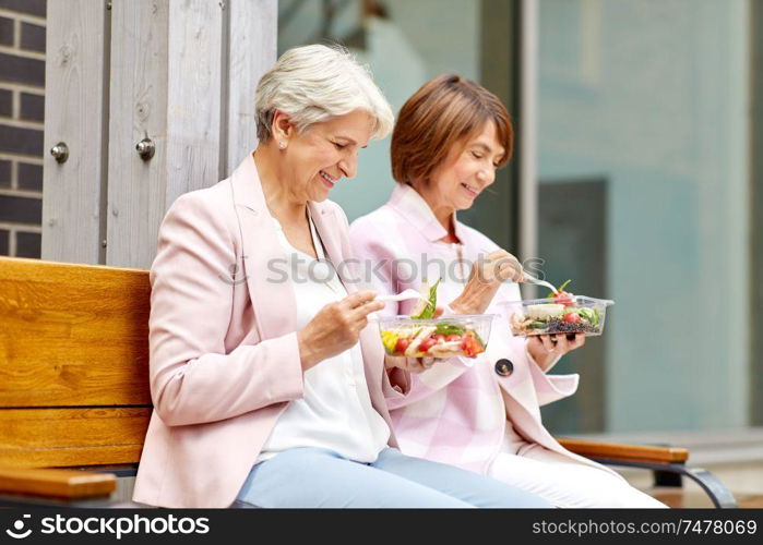 old age, leisure and food concept - senior women or friends eating takeaway salad on city street. senior women eating takeaway food on city street