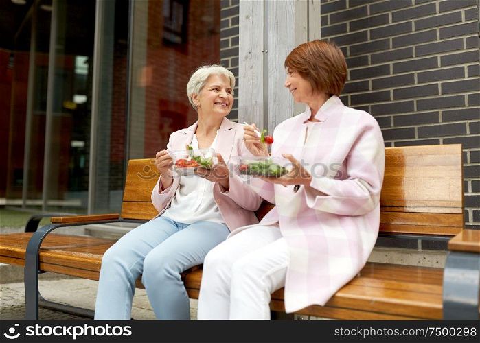 old age, leisure and food concept - senior women or friends eating takeaway salad on city street. senior women eating takeaway food on city street