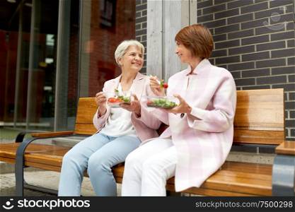 old age, leisure and food concept - senior women or friends eating takeaway salad on city street. senior women eating takeaway food on city street