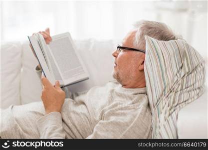 old age, leisure and people concept - senior man lying on sofa and reading book at home. senior man lying on sofa and reading book at home