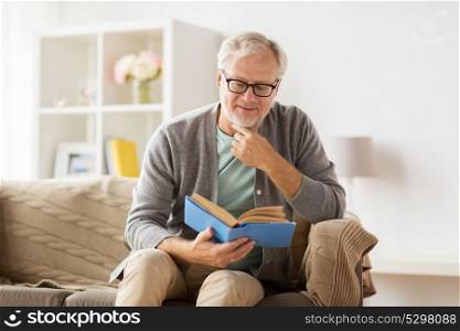 old age, leisure and people concept - senior man sitting on sofa and reading book at home. senior man on sofa reading book at home