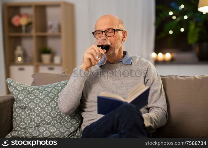 old age, leisure and people concept - senior man with book drinking red wine at home in evening. senior man with book drinking red wine at home