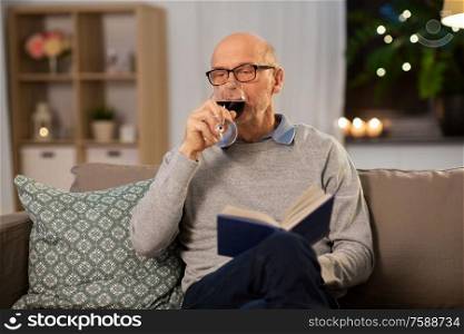old age, leisure and people concept - senior man with book drinking red wine at home in evening. senior man with book drinking red wine at home