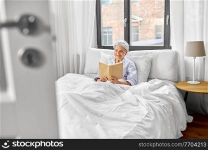 old age, leisure and people concept - senior woman reading book in bed at home bedroom. senior woman reading book in bed at home bedroom