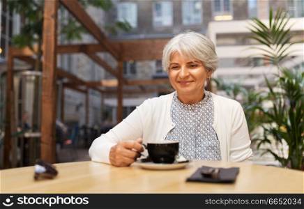 old age, leisure, retirement and people concept - happy senior woman drinking coffee at street cafe. senior woman drinking coffee at street cafe