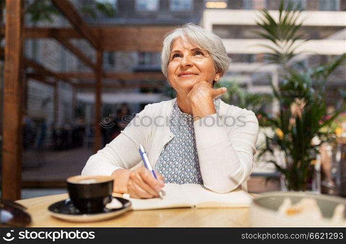 old age, leisure, retirement and people concept - happy senior woman with coffee and notebook dreaming at street cafe. senior woman with notebook dreaming at street cafe
