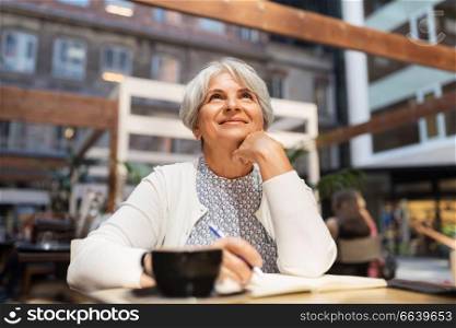 old age, leisure, retirement and people concept - happy senior woman with coffee and notebook dreaming at street cafe. senior woman with notebook dreaming at street cafe