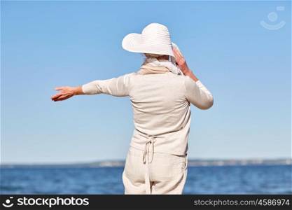 old age, leisure, travel, tourism and people concept - happy senior woman in sun hat on summer beach