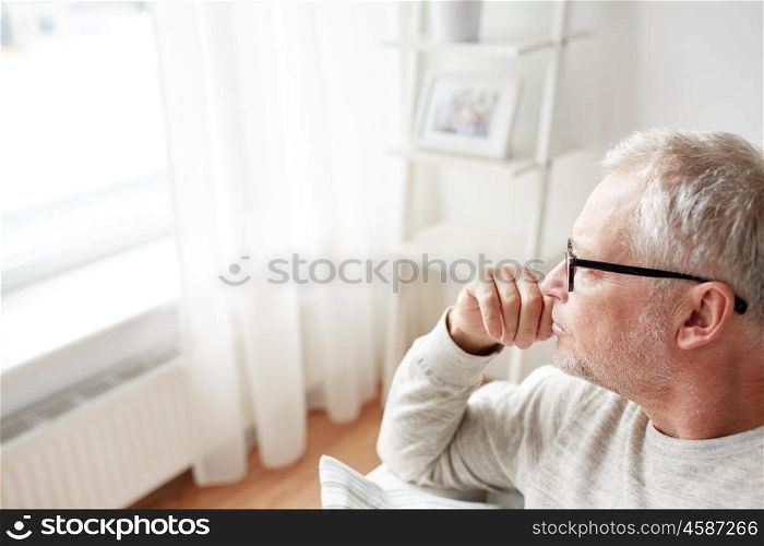 old age, lifestyle and people concept - close up of pensive senior man in glasses looking into window at home