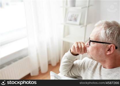 old age, lifestyle and people concept - close up of pensive senior man in glasses looking into window at home