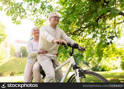 old age, people and lifestyle concept - happy senior couple riding together on bicycle at summer city park. happy senior couple riding on bicycle at park
