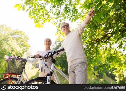 old age, people and lifestyle concept - happy senior couple walking with fixie bicycles at summer city park. happy senior couple with bicycles at summer park