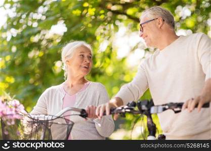 old age, people and lifestyle concept - happy senior couple walking with fixie bicycles talking at summer city park. happy senior couple with bicycles at summer park