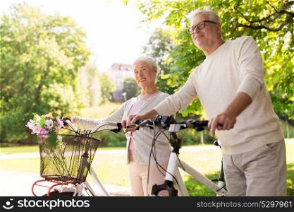 old age, people and lifestyle concept - happy senior couple walking with fixie bicycles at summer city park. happy senior couple with bicycles at summer park