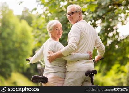 old age, people and lifestyle concept - happy senior couple with bicycles hugging at summer city park. happy senior couple with bicycles at summer park
