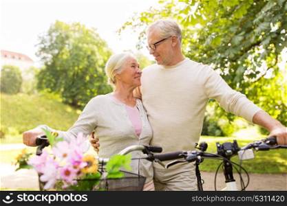 old age, people and lifestyle concept - happy senior couple with bicycles talking at summer city park. happy senior couple with bicycles at summer park