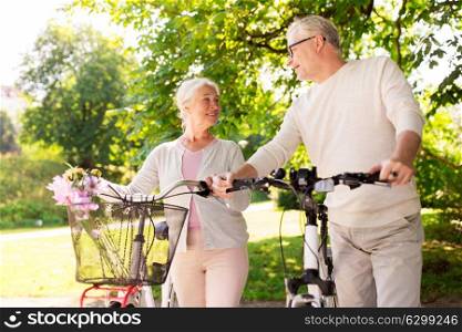 old age, people and lifestyle concept - happy senior couple with bicycles talking at summer city park. happy senior couple with bicycles at summer park
