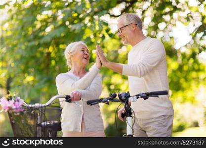 old age, people and lifestyle concept - happy senior couple with fixie bicycles making high five at summer city park. senior couple with bikes making high five at park