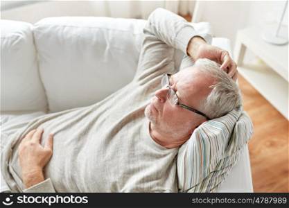 old age, problem and people concept - close up of senior man in glasses lying on sofa and thinking at home