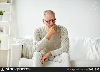 old age, problem and people concept - senior man in glasses thinking and sitting on sofa at home