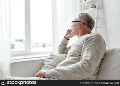 old age, problem and people concept - senior man in glasses thinking and looking through window at home