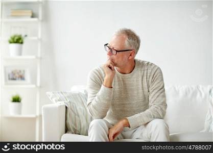 old age, problem and people concept - senior man in glasses thinking and sitting on sofa at home