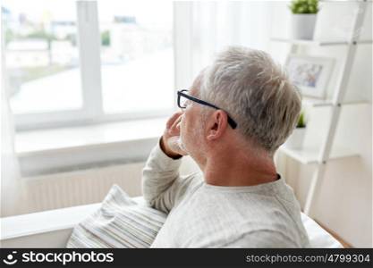 old age, problem and people concept - senior man in glasses thinking and looking through window at home