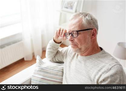 old age, problem and people concept - senior man sitting on sofa at home and thinking