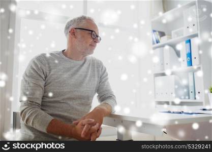 old age, problem, healthcare and people concept - sad senior man sitting at table at medical office over snow. senior man sitting at medical office table