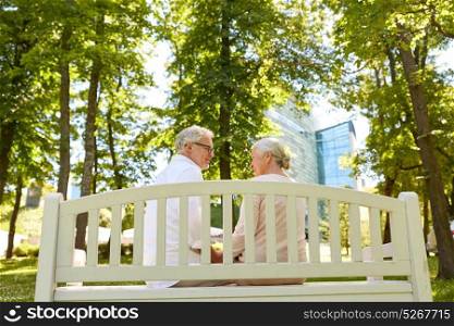 old age, relationship and people concept - happy senior couple sitting on bench at summer city park. happy senior couple sitting on bench at park