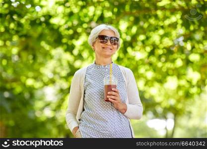 old age, retirement and people concept - close up of happy senior woman drinking takeaway shake or smoothie at summer park. senior woman drinking takeaway shake at park