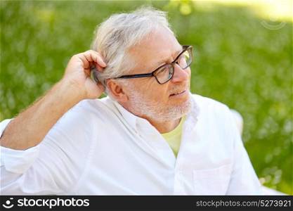 old age, retirement and people concept - happy senior man in glasses sitting at summer park. happy senior man in glasses sitting at summer park