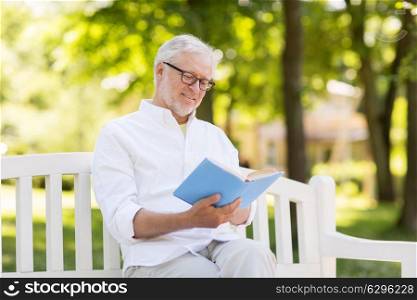 old age, retirement and people concept - happy senior man reading book sitting on bench at summer park. happy senior man reading book at summer park