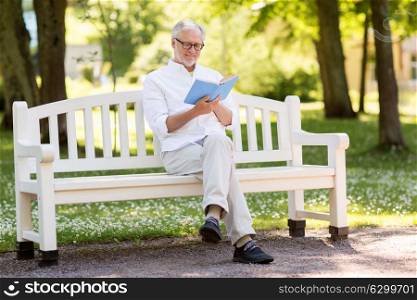 old age, retirement and people concept - happy senior man reading book sitting on bench at summer park. happy senior man reading book at summer park