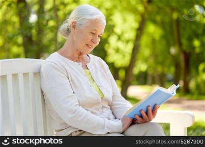 old age, retirement and people concept - happy senior woman reading book sitting on bench at summer park. happy senior woman reading book at summer park