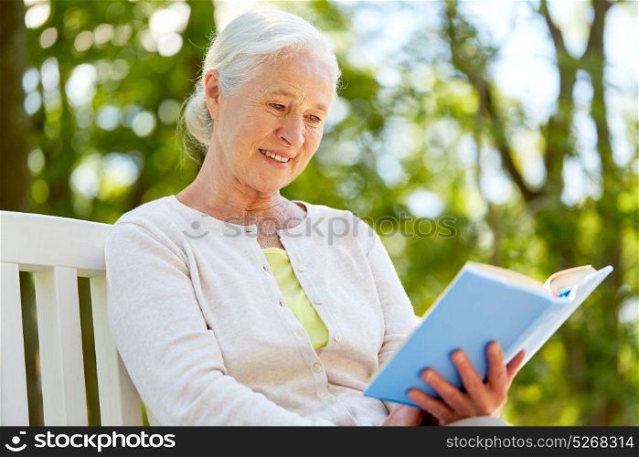 old age, retirement and people concept - happy senior woman reading book sitting on bench at summer park. happy senior woman reading book at summer park